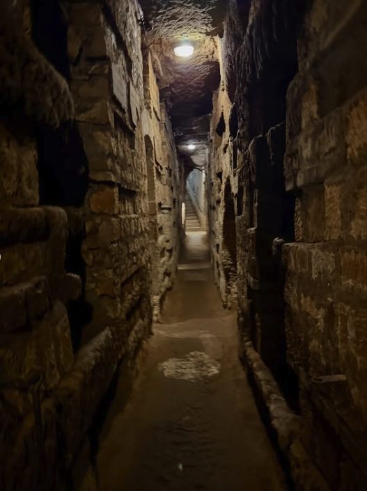 A lamplit gallery of empty loculi in the Rome Catacombs