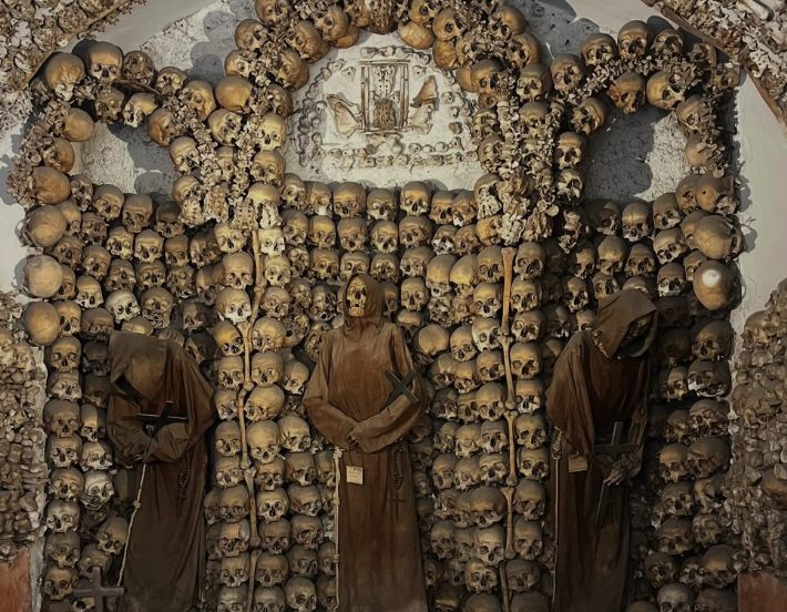 The Capuchin Crypt bone chapel, robed friars standing against walls of arranged skulls